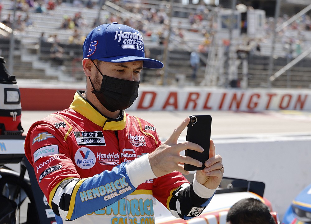 FILE - In this Sunday, May 9, 2021, file photo, Kyle Larson uses his cell phone before the NASCAR Cup Series auto race at Darlington Raceway in Darlington, S.C. Larson took time out from his NASCAR schedule to Zoom in with the class at Philadelphia’s Urban Youth Racing School. The Philly-based program that creates opportunities in racing for minorities extended an olive branch last year to Larson after the driver was caught using a slur during an iRacing event in April.(AP Photo/Terry Renna, File)