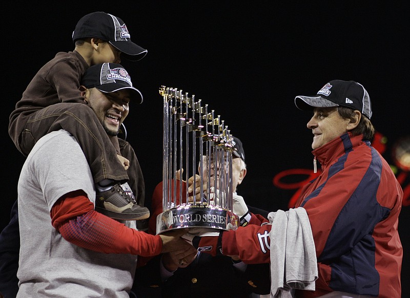 FILE - St. Louis Cardinals first baseman Albert Pujols, with his son A.J. Alberto Jr. on his shoulders, holds onto the World Series trophy with Cardinals manager Tony La Russa, right and General Manager Walt Jocketty, second right, after winning Game 5 of the World Series against the Detroit Tigers in St. Louis, in this Friday, Oct. 27, 2006, file photo. Pujols has been designated for assignment by the Los Angeles Angels, abruptly ending the 41-year-old superstar slugger's decade with his second major league team. The Angels announced the move Thursday, May 6, 2021, a day after Pujols wasn't in their lineup for their fourth consecutive loss.  (AP Photo/Elise Amendola, File)