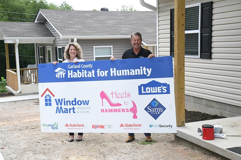 Courtney Post, Garland County Habitat for Humanity public relations coordinator, left, and Dennis Cooper, director of community engagement, hold a sign for Heels to Hammers at 222 Eddiemee St. Both 222 and 226 Eddiemee will have sod put down on Thursday. - Photo by Tanner Newton of The Sentinel-Record