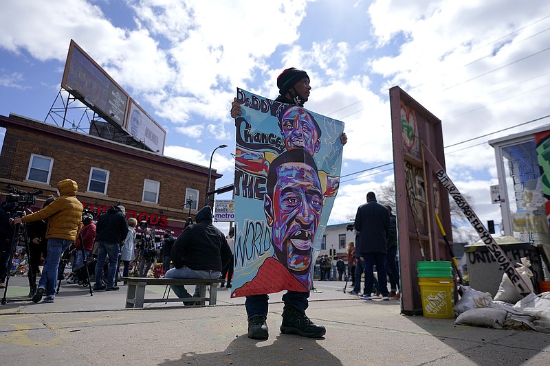 FILE - In this Wednesday, April 21, 2021, file photo, a man holds a sign at George Floyd Square, in Minneapolis, a day after former Minneapolis police Officer Derek Chauvin was convicted on all counts for the 2020 death of Floyd. The intersection where George Floyd took his final breaths was to be transformed Tuesday, May 25 into an outdoor festival on the one-year anniversary of his death, with food, children’s activities and a long list of musical performers. (AP Photo/Julio Cortez, File)