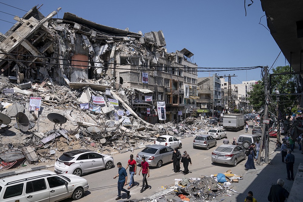 Motorists and pedestrians move past a building destroyed by an air-strike prior to a cease-fire that halted the 11-day war between Gaza's Hamas rulers and Israel, Tuesday, May 25, 2021, in Gaza City, the Gaza Strip. (AP Photo/John Minchillo)