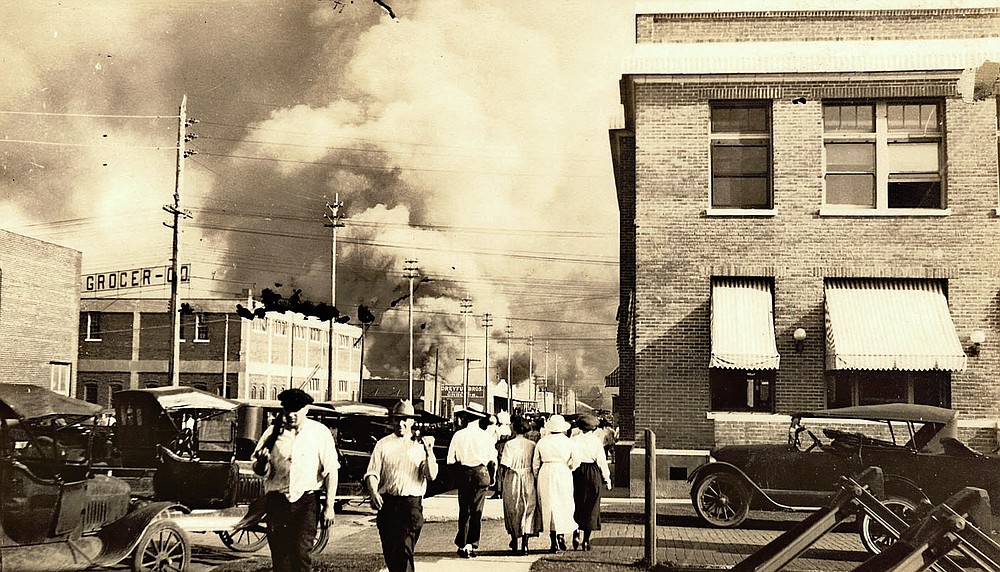 In this photo provided by Department of Special Collections, McFarlin Library, The University of Tulsa, two armed men in walk away from burning buildings as others walk in the opposite direction during the June 1, 1921, Tulsa Race Massacre in Tulsa, Okla. (Department of Special Collections, McFarlin Library, The University of Tulsa via AP)