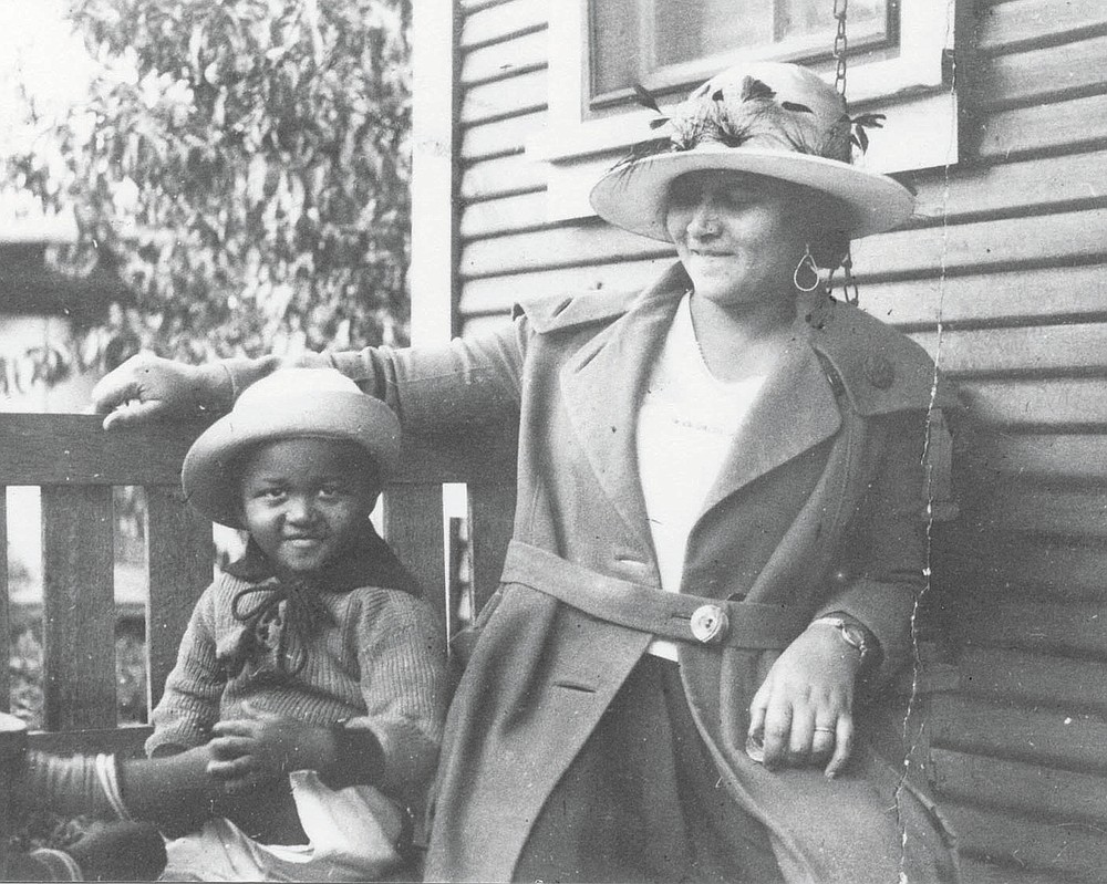 This photo provided by the Department of Special Collections, McFarlin Library, The University of Tulsa shows an African American woman and girl sitting on a porch swing, both dressed in coats and hats, by the side of a house. Provenance is unknown; however, it is believed that these photos were taken in Tulsa, Okla. prior to the Tulsa Race Massacre. (Department of Special Collections, McFarlin Library, The University of Tulsa via AP)