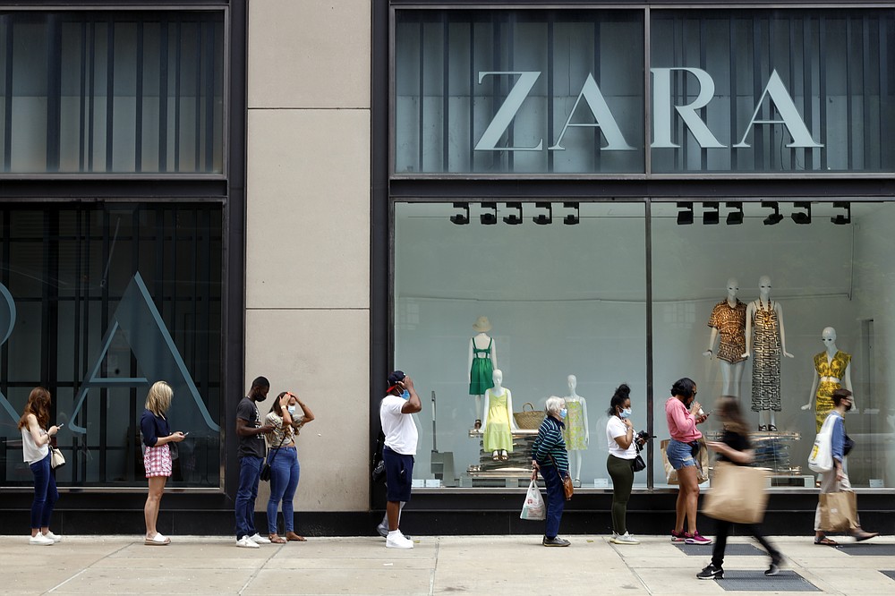 Shoppers wait in line outside a Chicago downtown retail store as others pass by, Wednesday, May 26, 2021. With vaccinations rolling out and shoppers freer to go out maskless, retailers are seeing an eager return to their stores after months of watching their customers focus on online buying during the pandemic. (AP Photo/Shafkat Anowar)