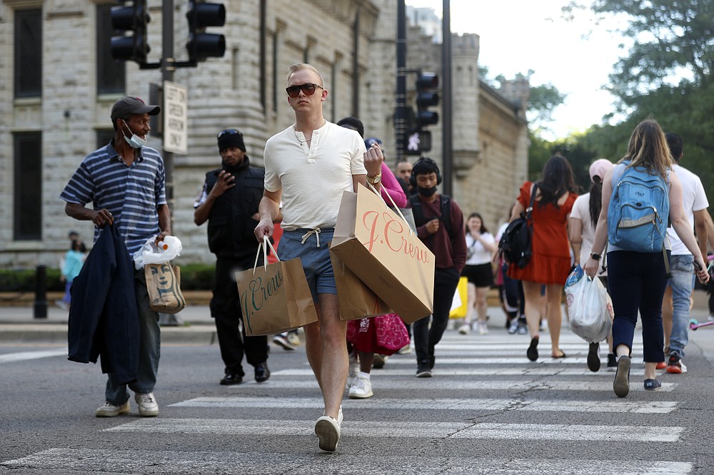 Troy Hemlin visiting Chicago from Springfield Il., crosses the street carrying shopping bags, Wednesday, May 26, 2021, in downtown Chicago. Americans are going back to one of their favorite past times: store shopping. With vaccinations rolling out and shoppers freer to go out maskless, retailers are seeing an eager return to their stores after months of watching their customers focus on online buying during the pandemic. (AP Photo/Shafkat Anowar)