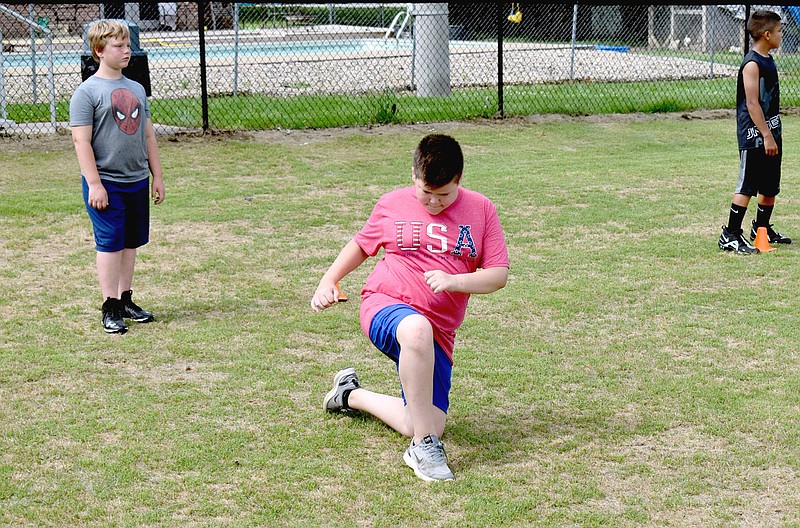 MARK HUMPHREY  ENTERPRISE-LEADER/Prairie Grove rising seventh grader Asher Taylor (center) works on perfecting football skills while Kristopher Phipps (left), a rising sixth grader; and Aiden Wilson, a rising seventh grader, await their turns during a Prairie Grove's annual pee wee football camp held last week.