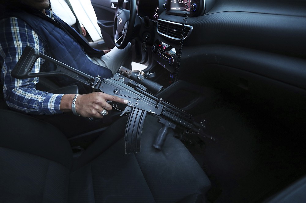 A government-assigned bodyguard for mayoral candidate Guillermo Valencia grabs his assault rifle in his vehicle during one of the PRI candidate's campaign stops in Morelia, Michoacan state, Mexico, Saturday, May 22, 2021. President Andres Manuel Lopez Obrador started the program to protect candidates, acknowledging that violence against candidates is alarming. (AP Photo/Marco Ugarte)