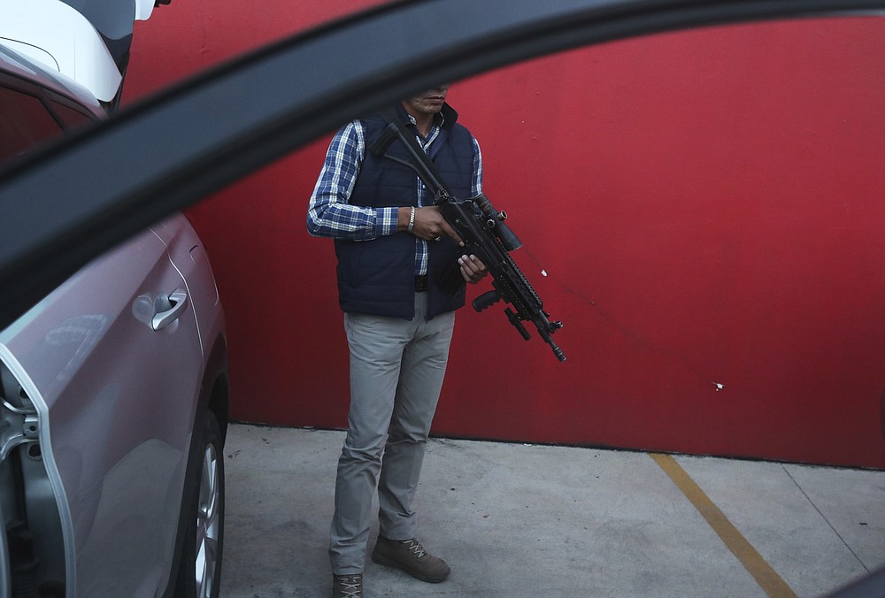 A government-assigned bodyguard for mayoral candidate Guillermo Valencia stands ready during one of the PRI candidate's campaign stops in Morelia, Michoacan state, Mexico, Saturday, May 22, 2021. President Andres Manuel Lopez Obrador started the program to protect candidates, acknowledging that violence against candidates is alarming. (AP Photo/Marco Ugarte)