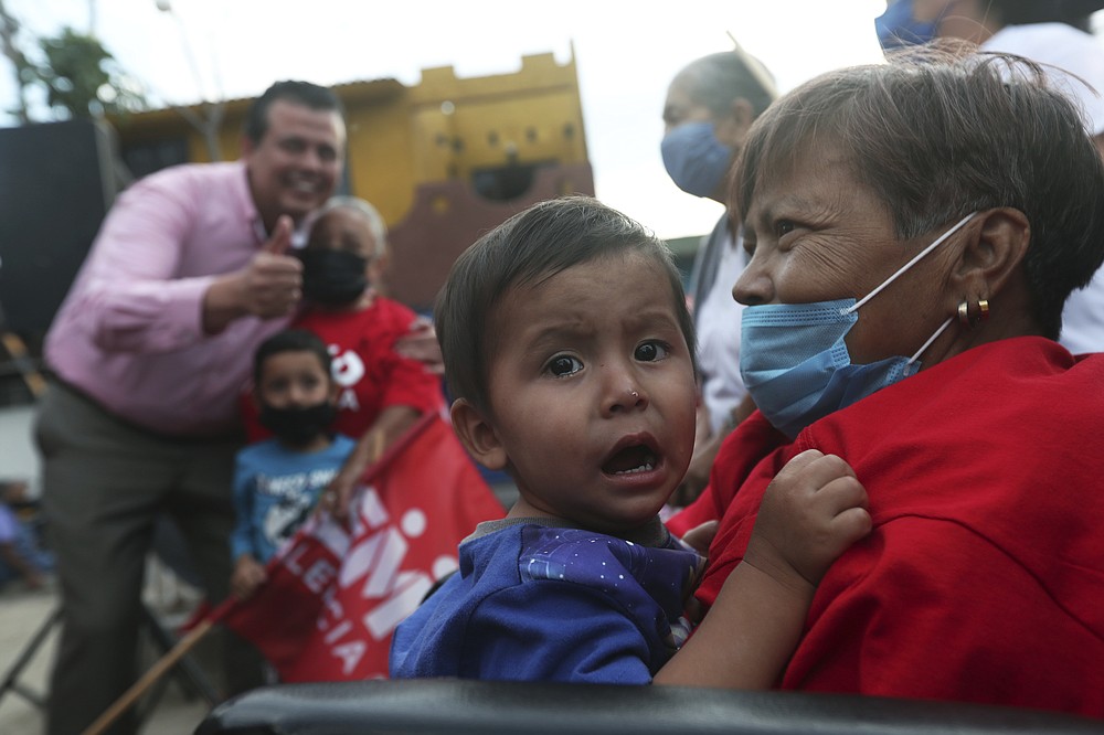 Supporters of mayoral candidate Guillermo Valencia, behind, attend a campaign event in Morelia, Michoacan state, Mexico, Friday, May 21, 2021. After a May 8 attack on his life that wounded his bodyguard and private secretary, the PRI candidate fears cartel gunmen will try to finish the job they botched. (AP Photo/Marco Ugarte)