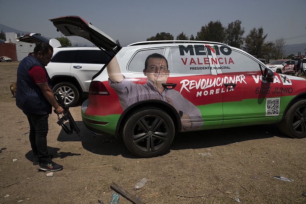One of the bodyguards that acts as the driver of Institutional Revolutionary Party, PRI, mayoral candidate Guillermo Valencia, grabs his assault rifle from the back of the armored SUV they travel in, during one of Valencia's campaign stops in Morelia, Michoacan state, Mexico, Saturday, May 22, 2021. The armored vehicle was loaned to Valencia by a friend after he was attacked by gunmen on May 8. (AP Photo/Marco Ugarte)