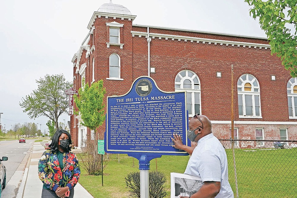 Chief Egunwale Amusan, right, and Tiffany Crutcher, left, talk about a sign commemorating the original Black Wall Street while on a tour given by Amusan, in Tulsa, Okla., on Monday, April 12, 2021. Crutcher says, terrorized by the Tulsa Race Massacre, “My father’s grandmother, Rebecca Brown Crutcher, had to flee Greenwood in fear of her life." But the family stayed in Tulsa, enduring some of the same post-massacre hardships that generations of Black Tulsans endured: urban renewal, inequality on the north side and police brutality. (AP Photo/Sue Ogrocki)