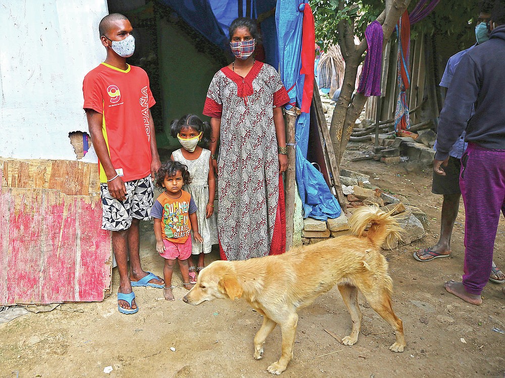 Gangaiah, left, son of Padmavathi who died of COVID-19, stands at the entrance of their family hut with his wife and children in a slum in Bengaluru, India, Thursday, May 20, 2021. Padmavathi collected hair, taking it from women's combs and hairbrushes to later be used for wigs. She earned about $50 a month. (AP Photo/Aijaz Rahi)