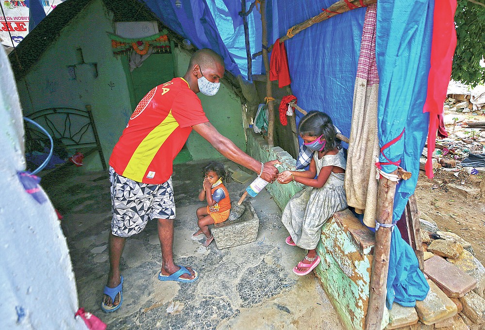Gangaiah, son of Padmavathi who died of COVID-19, gives sanitizer to his elder daughter Shanti as two-year-old Priya looks on inside their family hut which is made from bamboo and plastic sheeting at a slum in Bengaluru, India, Thursday, May 20, 2021. Padmavathi collected hair, taking it from women's combs and hairbrushes to later be used for wigs. She earned about $50 a month. (AP Photo/Aijaz Rahi)