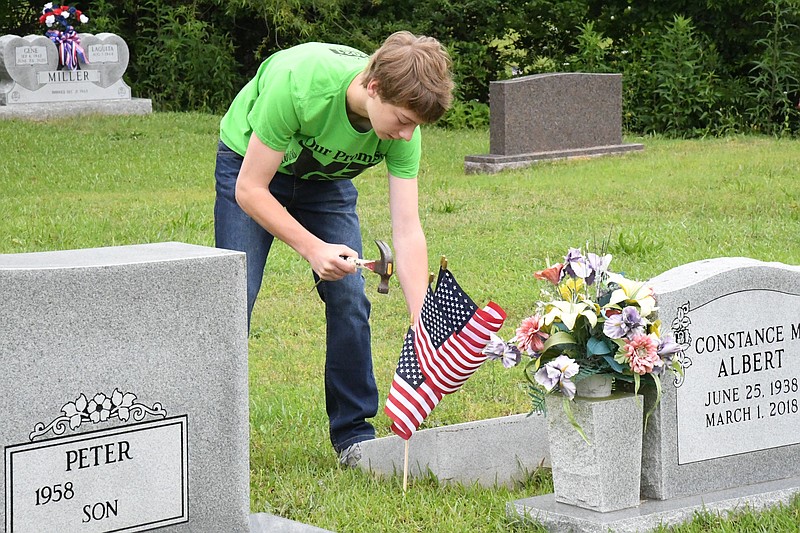 Yancy Rainwater, with Young Men of Distinction, hammers American flags into the ground next to veterans’ graves at Greenwood Cemetery on Saturday in preparation for Memorial Day. - Photo by Tanner Newton of The Sentinel-Record