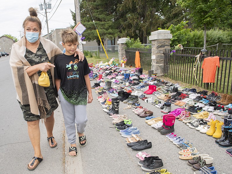 Lynn Karonhia-Beauvais and grandson Jamieson Kane walk past shoes representing the remains of 215 children outside St. Francis Xavier Church in Kahnawake, Quebec, Sunday, May 30, 2021. The remains of 215 children, some as young as 3 years old, have been found buried on the site of what was once Canada's largest Indigenous residential school — one of the institutions that held children taken from families across the nation. (Graham Hughes/The Canadian Press via AP)