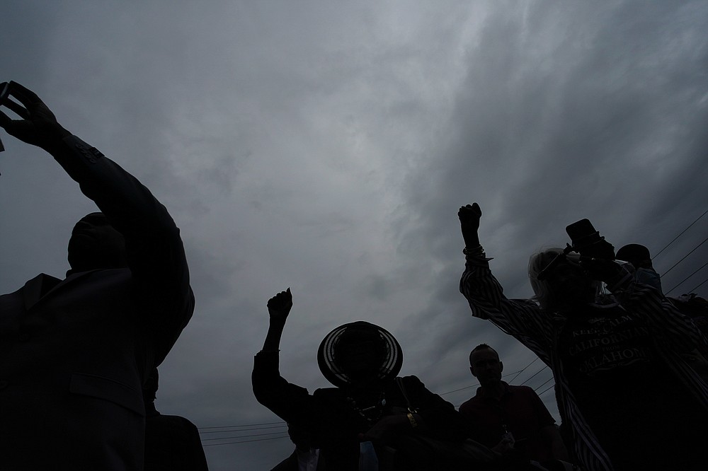 People raise up their arms during the dedication of a prayer wall outside of the historic Vernon African Methodist Episcopal Church in the Greenwood neighborhood during the centennial of the Tulsa Race Massacre, Monday, May 31, 2021, in Tulsa, Okla. The church was largely destroyed when a white mob descended on the prosperous Black neighborhood in 1921, burning, killing, looting and leveling a 35-square-block area. (AP Photo/John Locher)