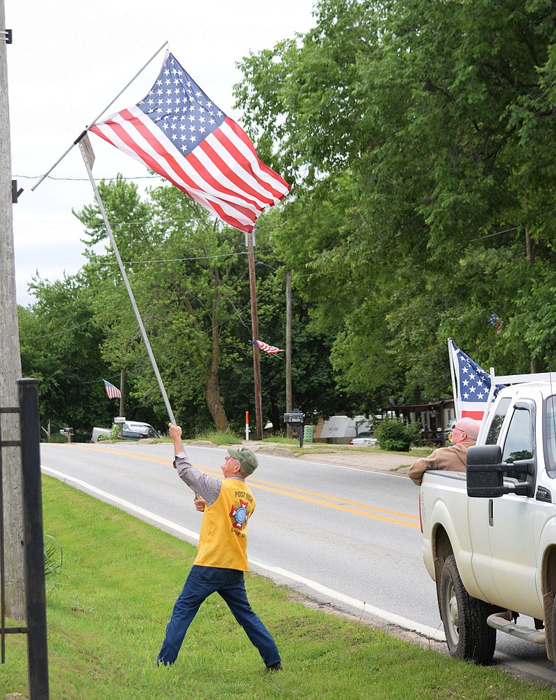 Westside Eagle Observer/MIKE ECKELS
A member of Howard-Parrish Veterans of Foreign Wars Post 9834 uses a special pole to hang the American flag on a light pole on Roller Avenue in Decatur Saturday morning as families and friends gather together to observer the 2021 Memorial Day weekend.