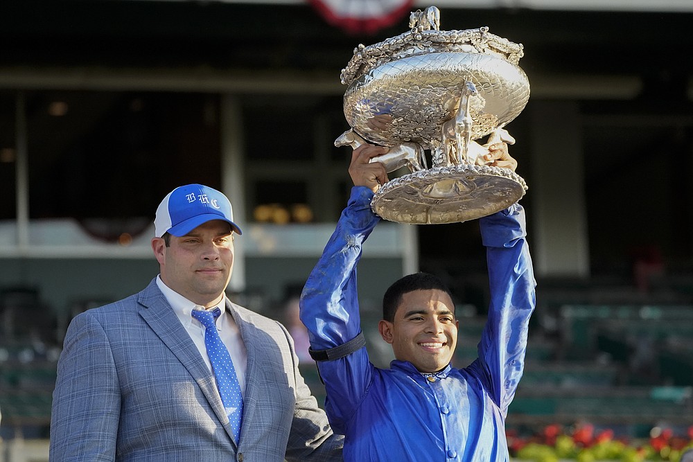 Jockey Luis Saez, right, holds up the August Belmont Trophy with Brad Cox after winning the 153rd running of the Belmont Stakes horse race with Essential Quality (2), Saturday, June 5, 2021, at Belmont Park in Elmont, N.Y. (AP Photo/Seth Wenig)