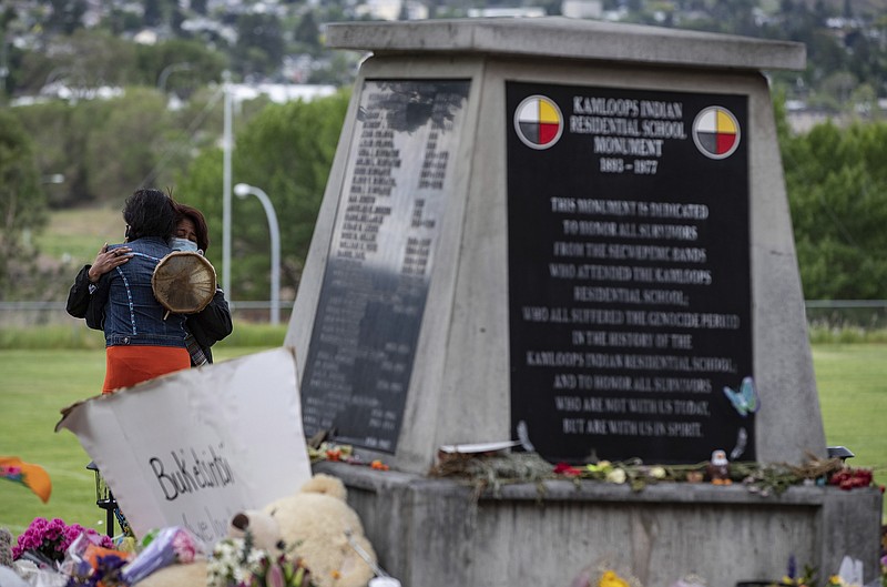 Two women embrace at a monument outside the former Kamloops Indian Residential School where flowers, cards and stuffed animals have been left as part of a growing makeshift memorial to honor the 215 children whose remains have been discovered buried near the facility, Friday, June 4, 2021 in Kamloops, British Columbia. (Darryl Dyck/The Canadian Press via AP)