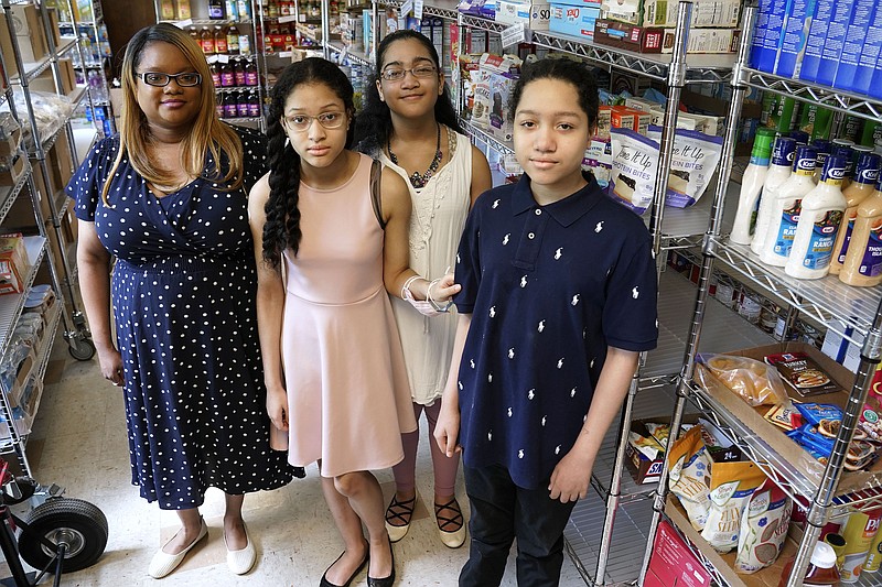 Aja Purnell-Mitchell, left, stands with her three children, Kyla, 13; Kyra, 15, and Cartier, 14, right, at a local food hub in Durham, N.C., on Friday, May 28, 2021, where they often help their mother. The teenagers have been learning remotely since last March but now plan to attend summer school after being vaccinated. (AP Photo/Gerry Broome)