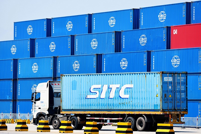 A container truck passes by stacks of COSCO containers on a dockyard of a port in Qingdao in eastern China's Shandong province Friday, June 4, 2021. China's exports surged nearly 28% in May while imports jumped 51% as demand rebounded in the U.S. and other markets where the pandemic is waning, though growth is leveling off after a stunning recovery from last year's slump. (Chinatopix via AP)
