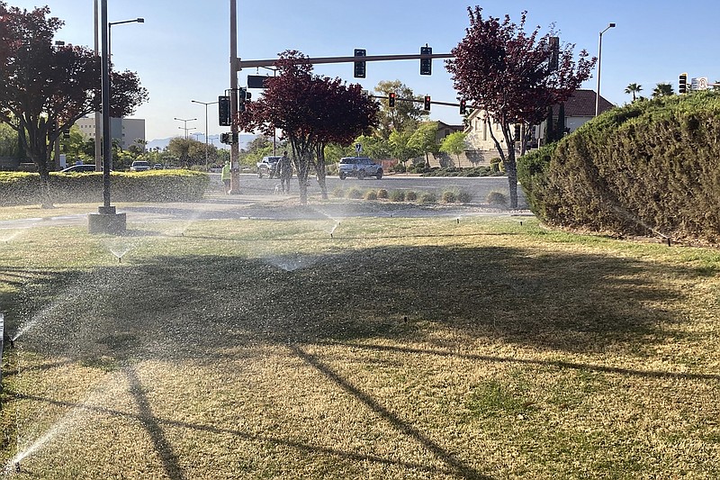 FILE - In this April 9, 2021, file photo, sprinklers water grass near a street corner in the Summerlin neighborhood of northwest Las Vegas. Nevada Gov. Steve Sisolak signed legislation on Friday, June 4 to make the state the first in the nation to ban certain kinds of grass. The measure will ban water users in southern Nevada from planting decorative grass in an effort to conserve water. (AP Photo/Ken Ritter, File)