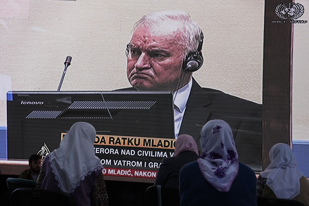 Women from Srebrenica watch a live broadcast from the Yugoslav War Crimes Tribunal in The Hague to learn the verdict for Bosnian Serb military chief Ratko Mladic, on the screen, at the memorial cemetery in Potocari near Srebrenica, eastern Bosnia, Tuesday, June 8, 2021. The United Nations court delivers its verdict in the appeal by former Bosnian Serb military chief Ratko Mladic against his convictions for genocide and other crimes and his life sentence for masterminding atrocities throughout the Bosnian war.(AP Photo/Darko Bandic)