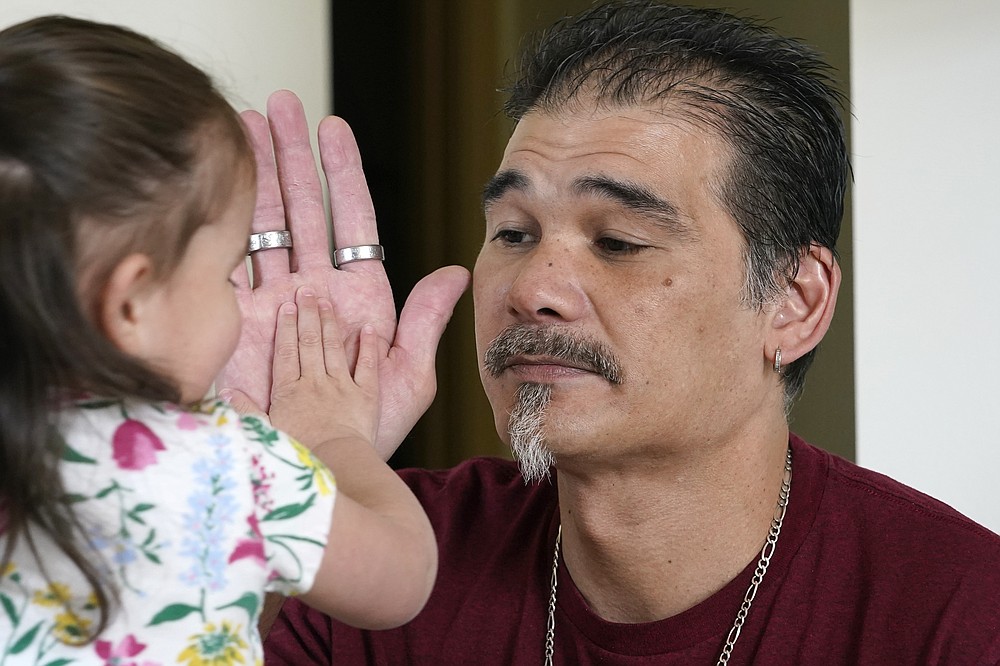 Leroy Pascubillo touches hands with his daughter, who was born addicted to heroin and placed with a foster family at birth, May 10, 2021, in Seattle. Pascubillo, who had used drugs for the better part of four decades, was in a court-ordered in-patient drug rehab program when the pandemic first hit. (AP Photo/Elaine Thompson)