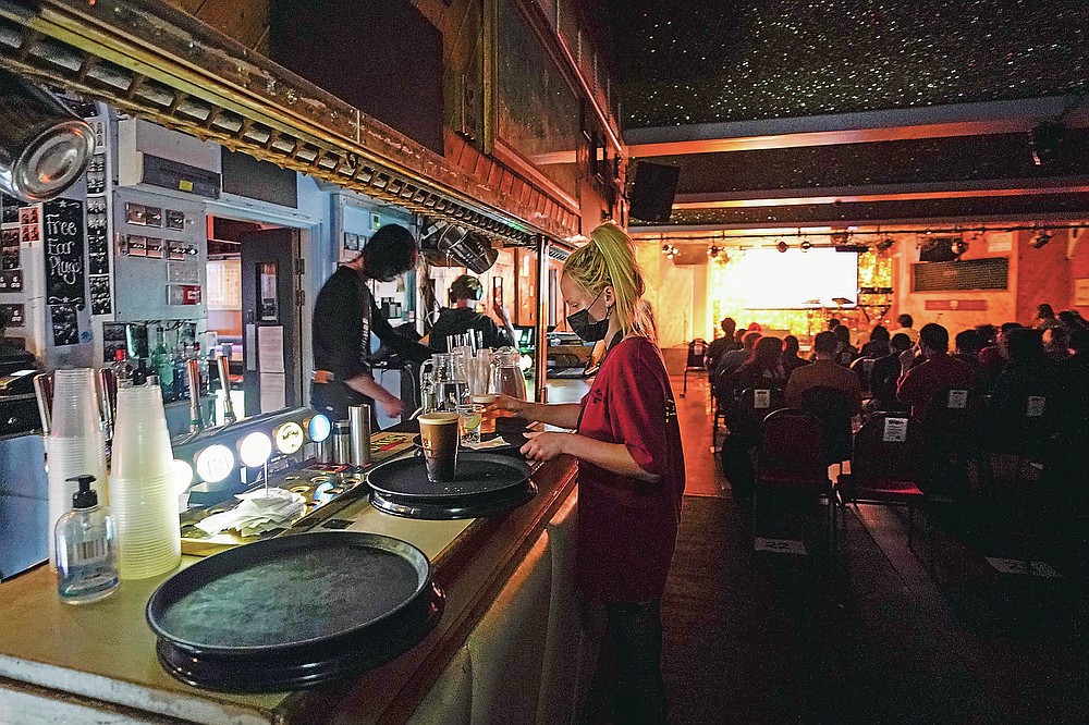 Una camarera recoge bebidas mientras lleva una mascarilla en el Moth Club en Hackney, antes de su show en vivo en el escenario, en Londres, el domingo 30 de mayo de 2021. El regreso de la música en vivo en la ciudad que produjo bandas desde los Rolling Stones hasta las Spice Girls han reavivado la creatividad de algunos de los muchos artistas que trabajan en Londres después de 14 meses de silencio. (Foto AP / Alberto Pezzali)