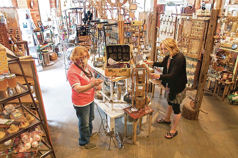 In this Thursday, May 21, 2020 photo, jewelry maker Joyce Greene, left, brings some of her one-of-a-kind jewelry to Finding Roots in Howell, Mich., as store co-owner Tirzah Sirken adjusts a display. (AP Photo/Livingston Daily Press and Argus, Gillis Benedict)