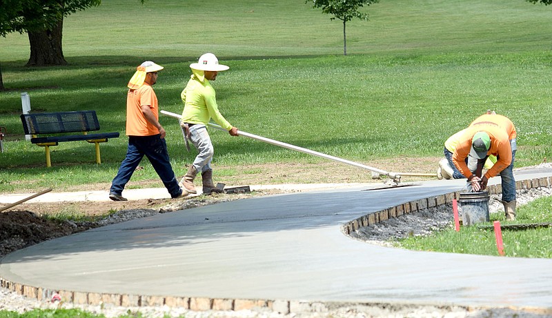 Westside Eagle Observer/MIKE ECKELS
Workers use trowels to smooth out freshly poured concrete on the corner connecting the old track to the walking trail near Pat Street June 9 at Decatur's Veterans Park. With the concrete work completed the loop was closed on the new walking trail.