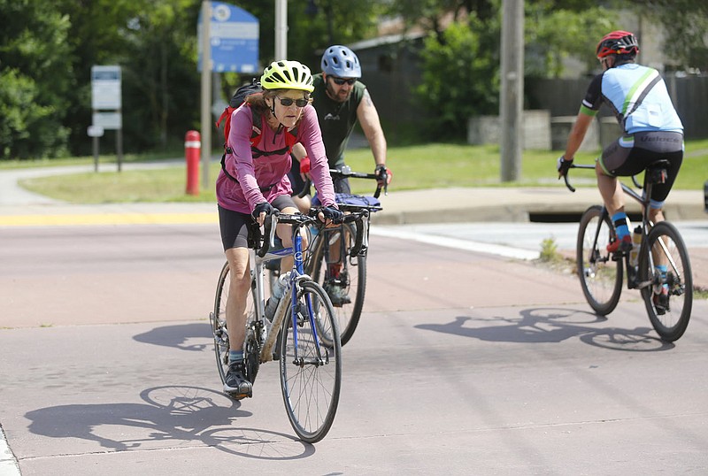 Karen Mowry (left), crosses Friday, June 11, 2021, W. North Street with other cyclist after the light change in Fayetteville. Cyclists and pedestrians are at an obvious disadvantage versus cars so engineers and planners are designing streets that make things safer by decreasing the chances of them coming into direct contact. Check out nwadg.com/photos for a photo gallery.
(NWA Democrat-Gazette/David Gottschalk)