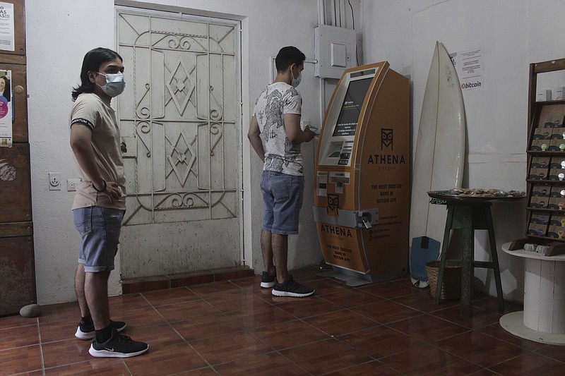 Eduardo Magaña, right, uses the first ATM designed to withdraw cash through the cryptocurrency App "Bitcoin Beach" on El Zonte Beach in Tamanique, El Salvador, Wednesday, June 9, 2021. In this beach community, a nongovernmental organization with the financial backing of an anonymous Bitcoin donor has been trying to create a small-scale cryptocurrency economy, and could serve as a showcase for the gains and struggles to introduce a phone-based cryptocurrency as the country embarks on a nationwide experiment after making Bitcoin legal tender this week. (AP Photo/Salvador Melendez)