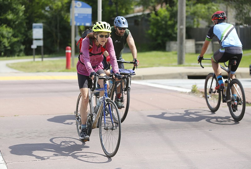Karen Mowry (left), crosses W. North Street with other cyclists Friday, June 11, 2021, after the light change in Fayetteville. Cyclists and pedestrians are at an obvious disadvantage versus cars, so engineers and planners are designing streets that make things safer by decreasing the chances of them coming into direct contact. Check out nwadg.com/photos for a photo gallery.
(NWA Democrat-Gazette/David Gottschalk)
