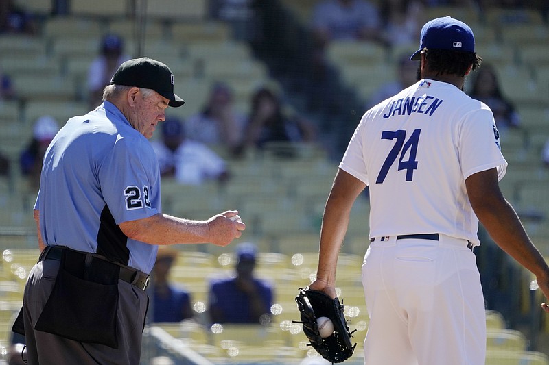 In this Sunday, June 13, 2021, photo, home plate umpire Joe West, left, takes a look at the ball that Los Angeles Dodgers relief pitcher Kenley Jansen had been using after giving him a fresh one during the ninth inning of a baseball game between the Dodgers and the Texas Rangers in Los Angeles. Pitchers will be ejected and suspended for 10 games for using illegal foreign substances to doctor baseballs in a crackdown by Major League Baseball that will start June 21. (AP Photo/Mark J. Terrill, File)