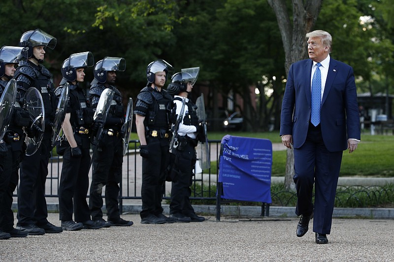 FILE - In this June 1, 2020 file photo, President Donald Trump walks past police in Lafayette Park after visiting outside St. John's Church across from the White House in Washington. An internal investigation has determined that the decision to clear racial justice protestors from an area in front of the White House last summer was not influenced by then-President Donald Trump’s plans for a photo opportunity at that spot. The report released Wednesday by the Department of Interior’s Inspector General concludes that the protestors were cleared by U.S. Park Police on June 1 of last year so new fencing could be installed.  (AP Photo/Patrick Semansky)