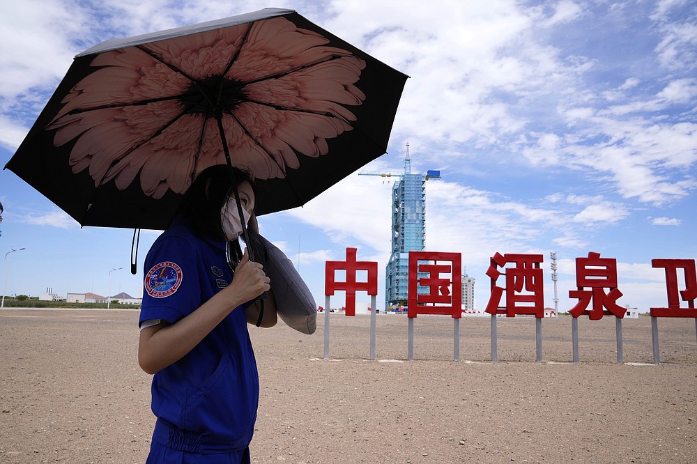 A worker holds an umbrella near the Shenzhou-12 spacecraft covered on the launch pad with the Chinese characters reading "China Jiuquan Satellite Launch Center" near Jiuquan on Wednesday, June 16, 2021. China plans to launch three astronauts onboard the Shenzhou-12 spacecraft, who will be the first crew members to live on China's new orbiting space station Tianhe, or Heavenly Harmony, from the Jiuquan Satellite Launch Center in northwest China.  (AP Photo/Ng Han Guan)