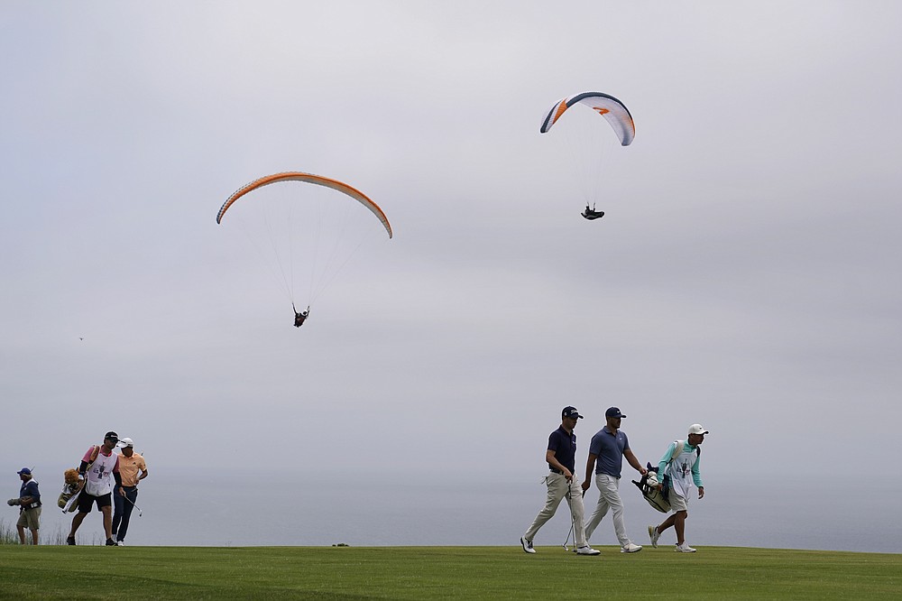 Brooks Koepka, left, and Justin Thomas walk along the fourth fairway as paragliders sail over the Pacific Ocean during the second round of the U.S. Open Golf Championship, Friday, June 18, 2021, at Torrey Pines Golf Course in San Diego. (AP Photo/Marcio Jose Sanchez)