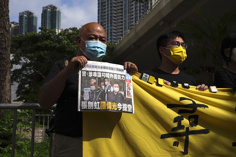 Pro-democracy activists holding a copy of Apple Daily newspaper and banner protest outside a court in Hong Kong, Saturday, June 19, 2021, to demand to release political prisoners. The top editor of the Hong Kong's pro-democracy newspaper and the head of its parent company were brought to a courthouse Saturday for their first hearing since their arrest under the city's national security law.(AP Photo/Kin Cheung)