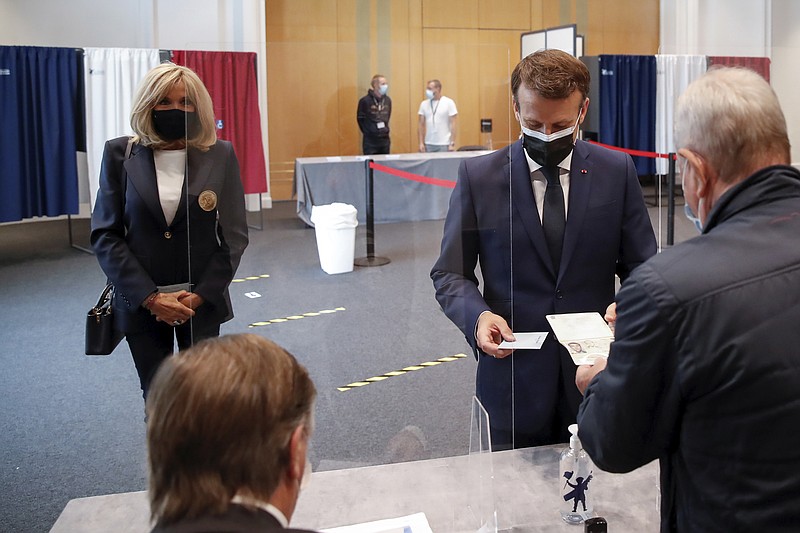 French President Emmanuel Macron shows his passport while his wife Brigitte waits during the first round of French regional and departmental elections, in Le Touquet-Paris-Plage, northern France, Sunday, June 20, 2021. The elections for leadership councils of France's 13 regions, from Brittany to Burgundy to the French Riviera, are primarily about local issues like transportation, schools and infrastructure. But leading politicians are using them as a platform to test ideas and win followers ahead of the April presidential election. (Christian Hartmann/Pool via AP)