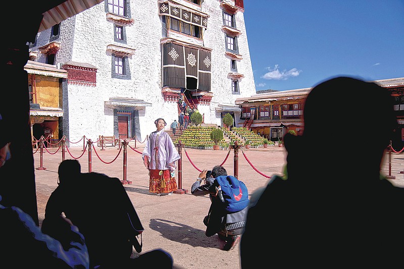 A Chinese tourist in Tibetan dress poses for a photo in a courtyard at the Potala Palace in Lhasa in western China's Tibet Autonomous Region, Tuesday, June 1, 2021. Tourism is booming in Tibet as more Chinese travel in-country because of the coronavirus pandemic, posing risks to the region's fragile environment and historic sites. (AP Photo/Mark Schiefelbein)