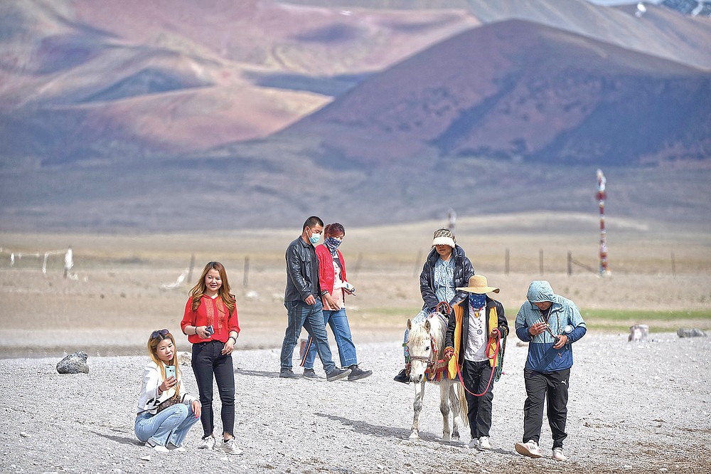 Touristen gehen am Seeufer entlang und reiten auf einem Pony in Namtso in der westchinesischen Autonomen Region Tibet, Mittwoch, 2. Juni 2021. Der Tourismus in Tibet boomt, da mehr Chinesen aufgrund der Coronavirus-Pandemie ins Land reisen, was die fragile Umwelt der Region gefährdet und historische Stätten.  (AP Foto/Mark Schiefebein)