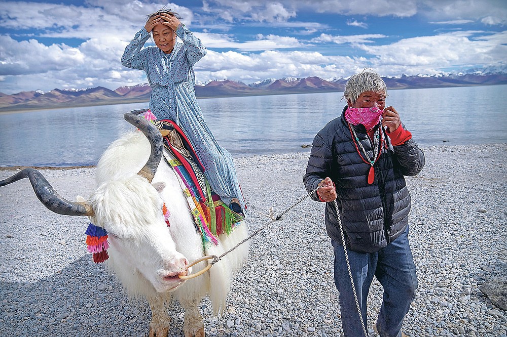 Ein chinesischer Tourist macht sich bereit, für ein Foto auf einem weißen Yak zu posieren, der von einem tibetischen Mann in Namtso in der westchinesischen Autonomen Region Tibet am Mittwoch, den 2. Juni 2021 geführt wird. Der Tourismus in Tibet boomt, da immer mehr Chinesen das Land bereisen die Coronavirus-Pandemie, die die fragile Umwelt und die historischen Stätten der Region gefährdet.  (AP Foto/Mark Schiefebein)