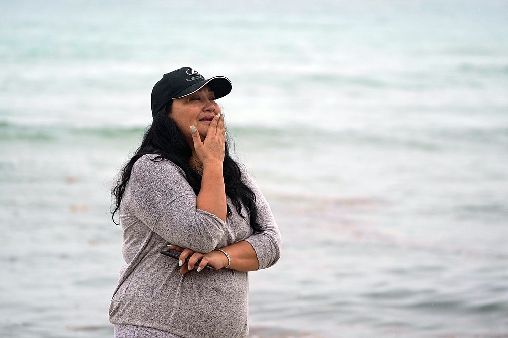 A woman reacts as she looks at a partially collapsed building, Thursday, June 24, 2021, in Surfside, Fla. A wing of a 12-story beachfront condo building collapsed with a roar in a town outside Miami early Thursday, trapping residents in rubble and twisted metal. (AP Photo/Wilfredo Lee)