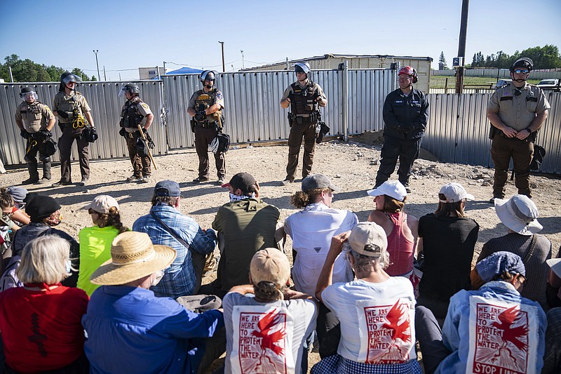Law enforcement agents form a line in front of a wall of protesters who sit just in front of a locked gate at an Enbridge pump station, Monday, June 7, 2021, in Hubbard County, Minn. Indigenous protesters and allies occupied the active site, some physically chaining themselves to equipment, forcing workers to leave, in protest of the construction of Enbridge Line 3. (Alex Kormann/Star Tribune via AP)