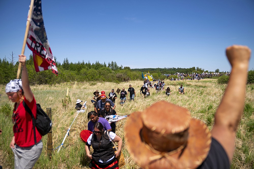 Indigenous leaders and "water protectors" march through swamp land to the boardwalk leading to an Enbridge pipeline construction site, on Monday, June 7, 2021, in Clearwater County, Minn. More than 2,000 Indigenous leaders and "water protectors" gathered in Clearwater County from around the country to protest the construction of Enbridge Line 3. The day started with a prayer circle and moved on to a march to the Mississippi headwaters where the oil pipeline is proposed to be built. (Alex Kormann/Star Tribune via AP)