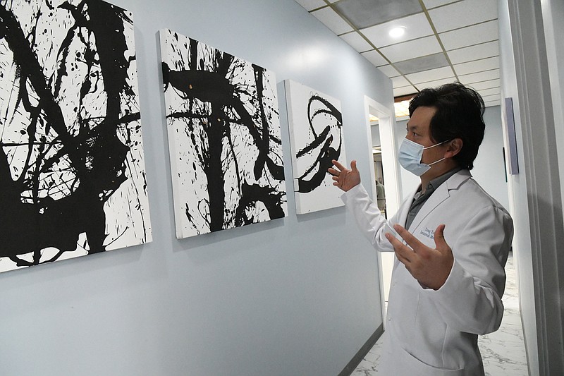 Dr. Yang Xu discusses artwork created by his father, Longhua Xu, that is on display in his new clinic. - Photo by Tanner Newton of The Sentinel-Record