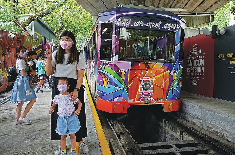 Passengers pose next to a Peak Tram on June 16, 2021. The Hong Kong Peak Tram is a staple in the memory of many residents and tourists, carrying passengers to Victoria Peak for a bird's-eye view of the many skyscrapers. city sky. (AP Photo / Vincent Yu)
