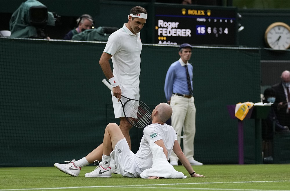 Elvețianul Roger Federer vorbește cu francezul Adrien Mannarino în timp ce se întinde pe podea în agonie în timpul meciului său din prima rundă masculină la prima zi a Campionatului de tenis de la Wimbledon de la Londra, marți, 29 iunie 2021 (Foto AP / Kirsty Wigglesworth)