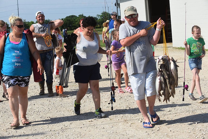 Mike Smyers (right) of Bentonville carries his family's stringer of channel catfish on Saturday June 12 2021 at the annual fishing derby held each June at the Charlie Craig State Fish Hatchery in Centerton operated by the Arkansas Game and Fish Commission. The derby is held each June in conjunction with Free Fishing Days in Arkansas, when residents and nonresidents may fish without a fishing license or trout stamp. 
(NWA Democrat-Gazette/Flip Putthoff)